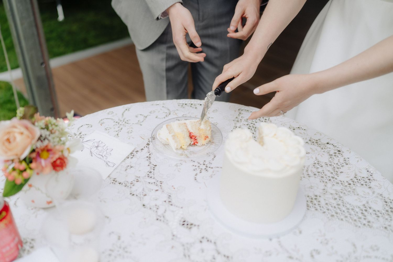 Close-up details of wedding cake cutting with white frosting on a lace tablecloth.