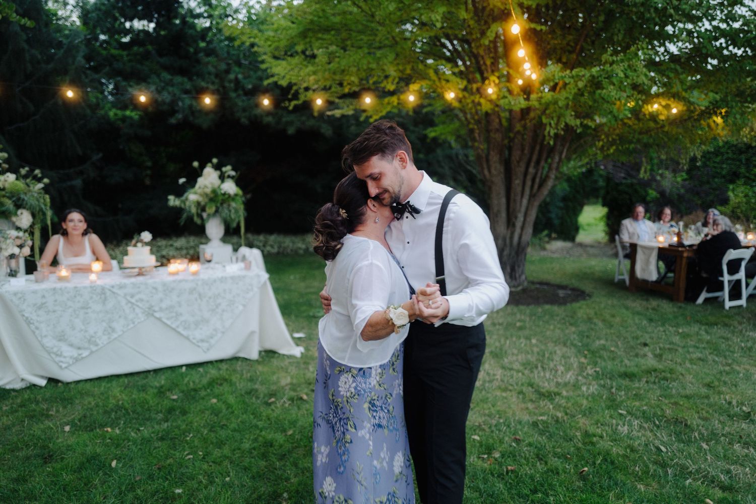 Outdoor wedding reception setup with string lights and garden ambiance at dusk.