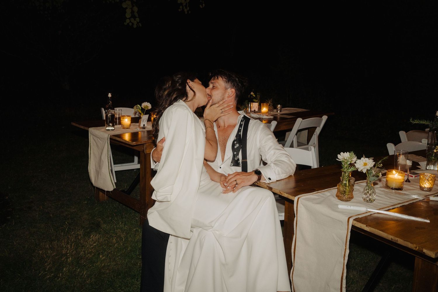 Intimate wedding reception dinner setup with candlelight and rustic decor in an outdoor setting.