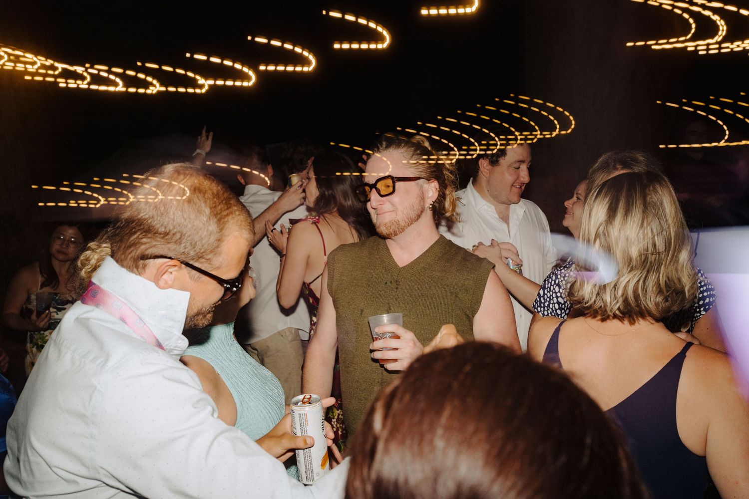 Party crowd dances under warm string lights at a lively nighttime celebration.