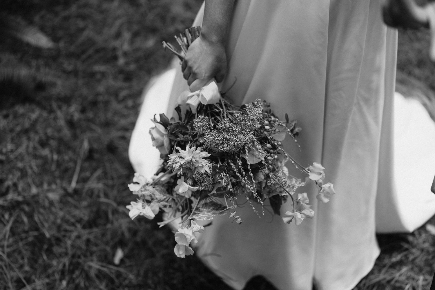 Black and white photo captures elegant wedding details including floral arrangements and dress fabric.