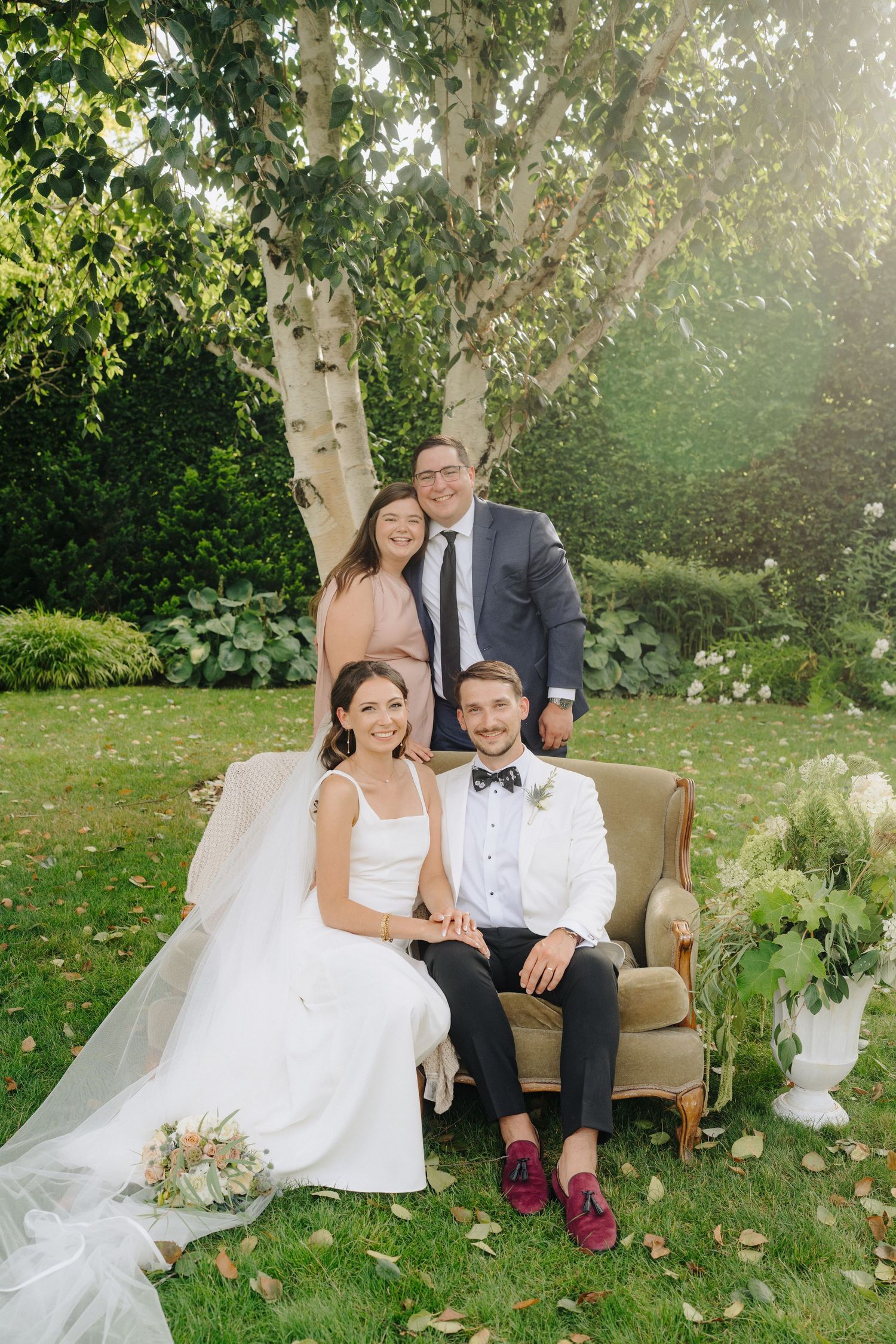 Elegant outdoor wedding seating arrangement with vintage armchair against birch trees and garden backdrop.
