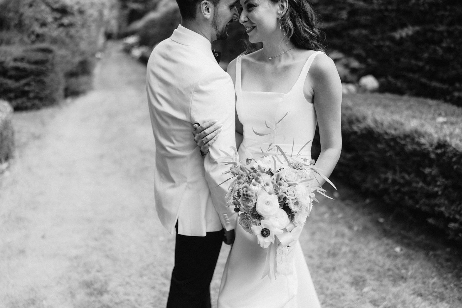 Romantic black and white portrait of couple embracing in garden setting.