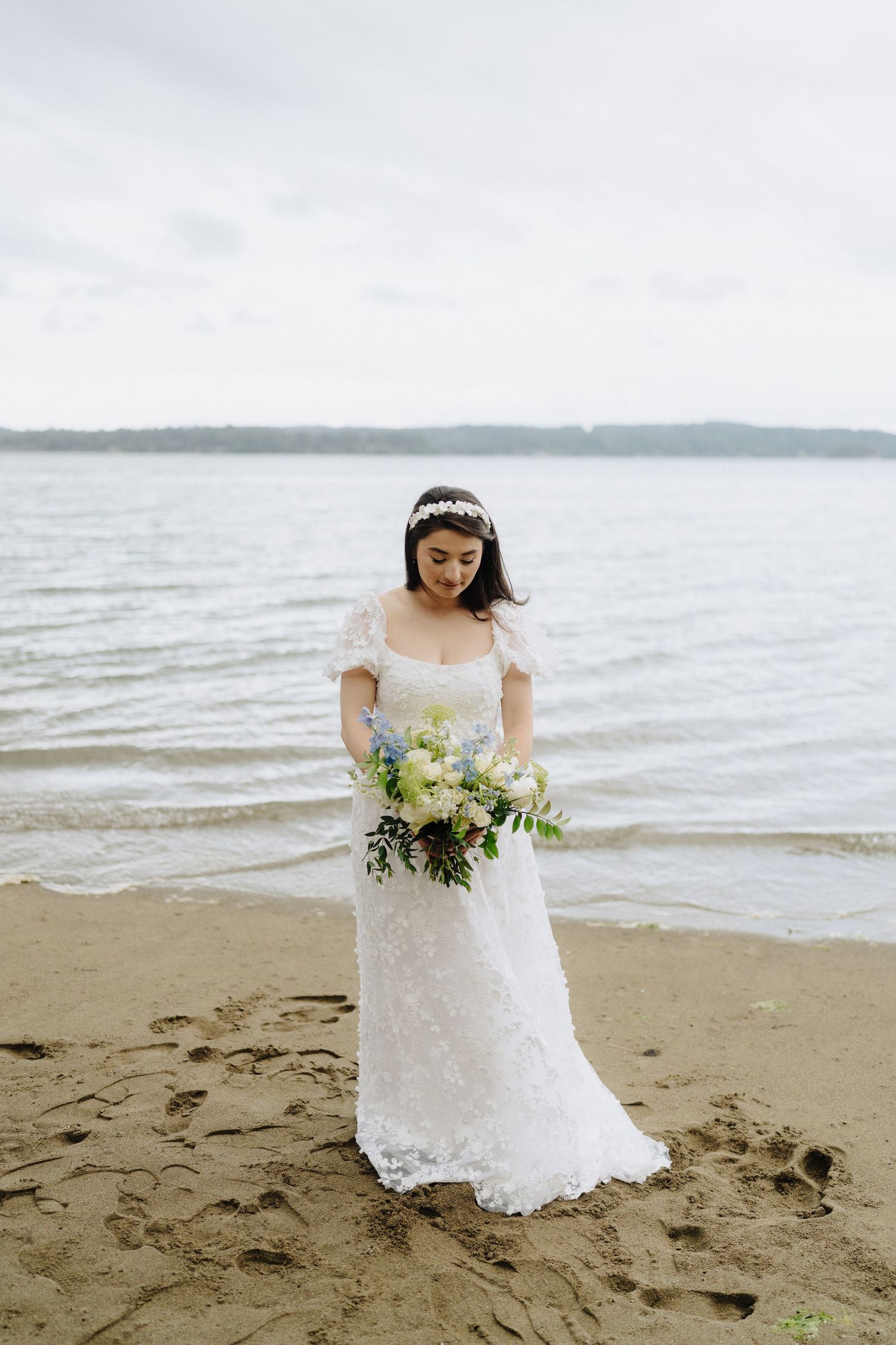 A white lace wedding dress and bouquet photographed against a scenic beach backdrop.