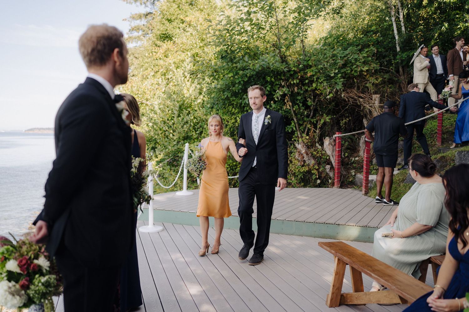 Wedding celebration on a waterfront deck with guests mingling during golden hour.