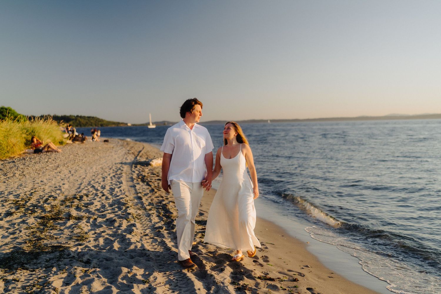 Couple strolling together on a sandy beach with ocean waves and sunset in the background.