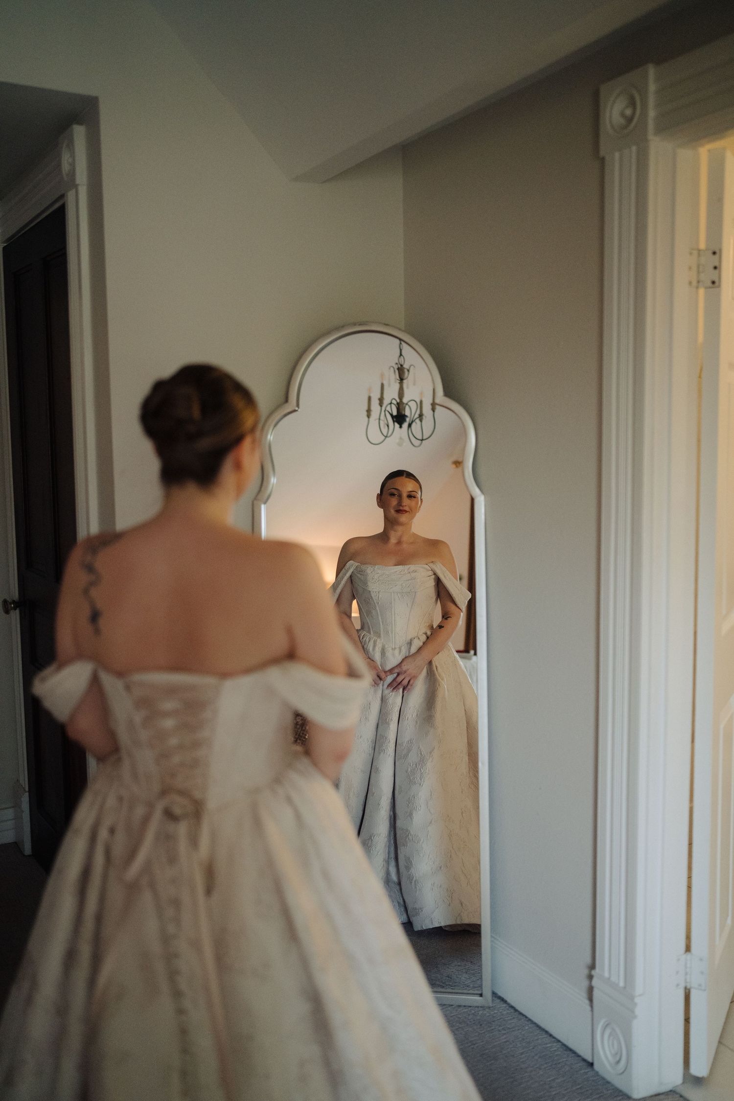A bride in a white wedding dress looks at her reflection in a vintage mirror.