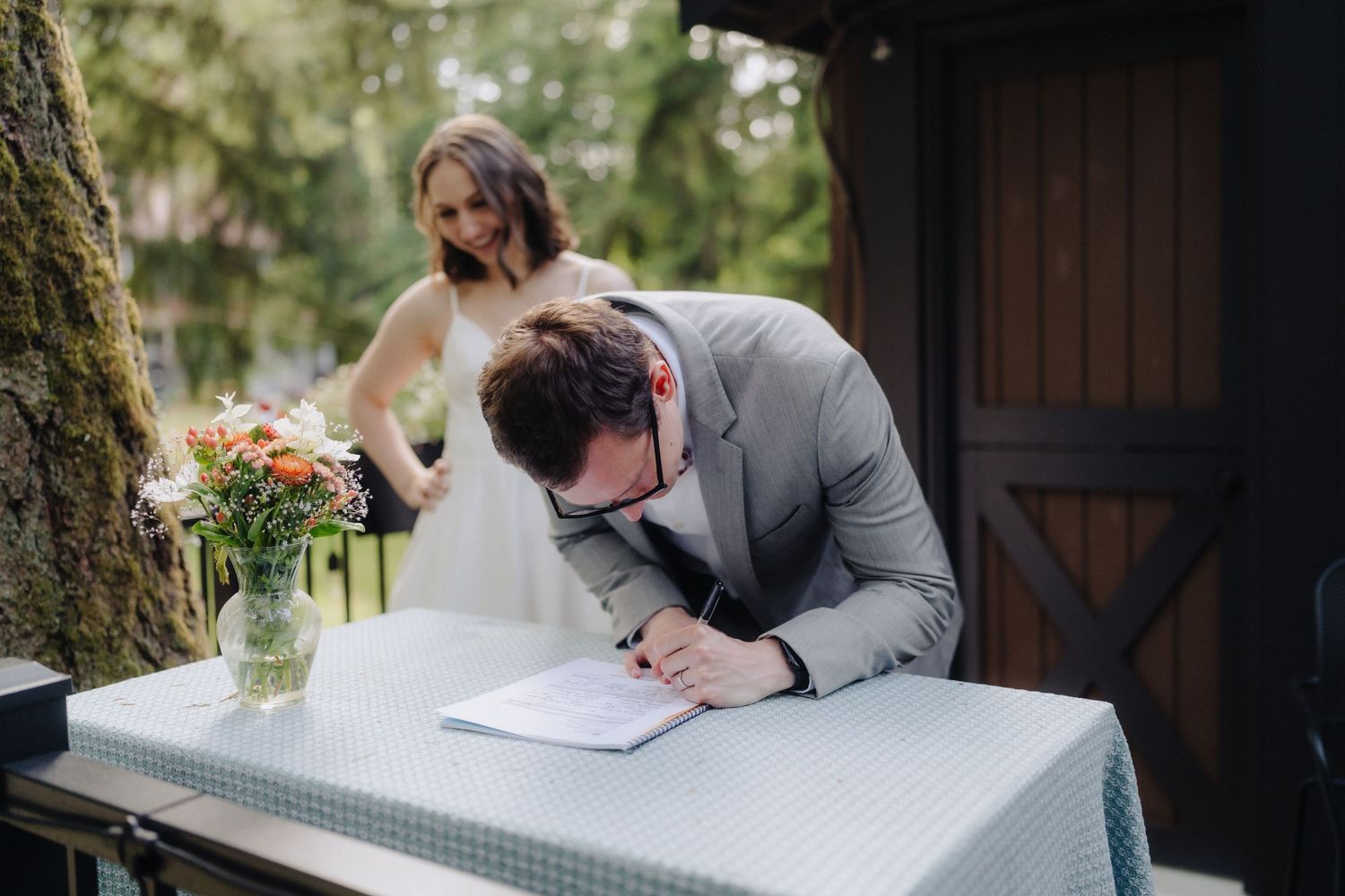 A couple signs their marriage license at an outdoor ceremony table.