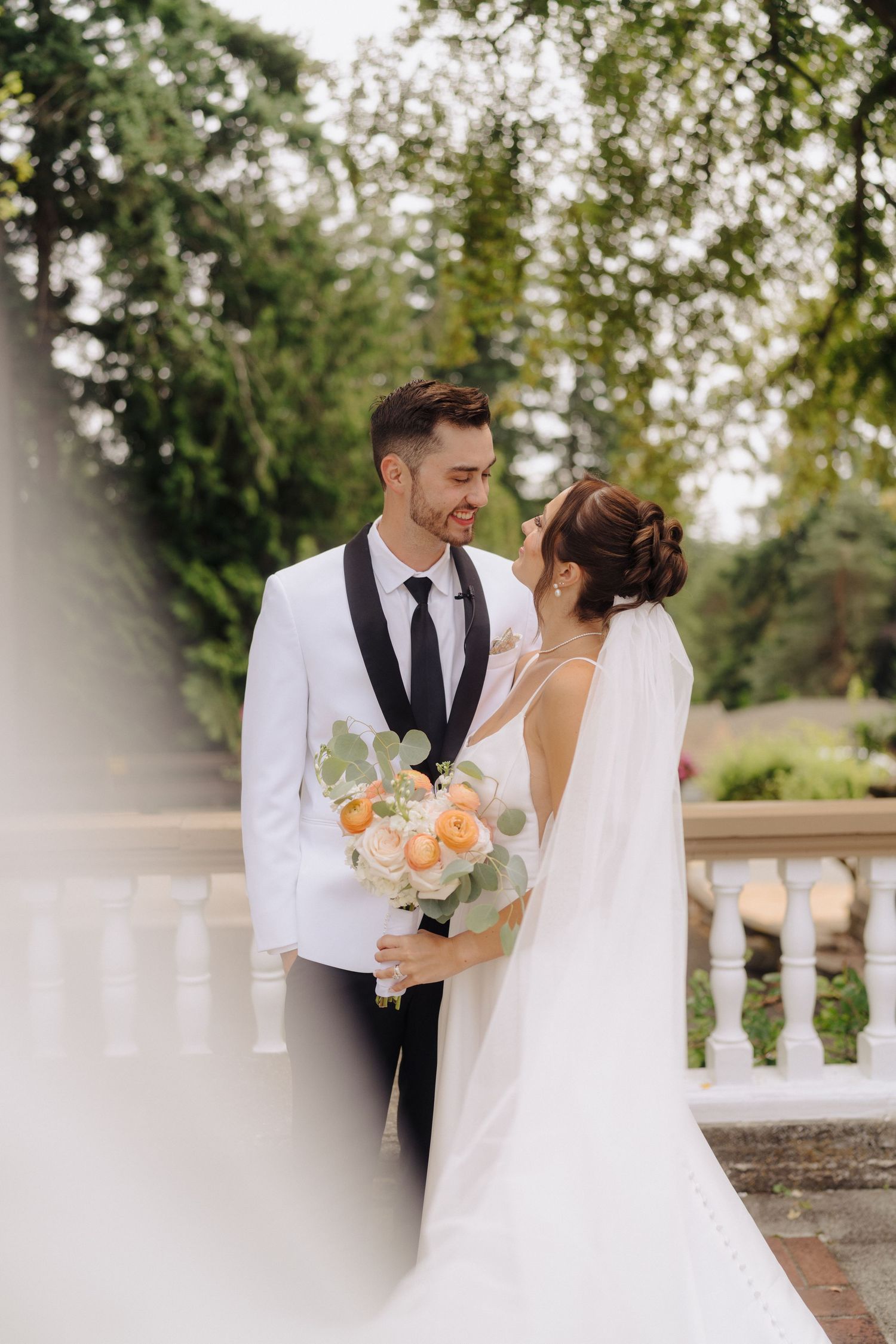 A romantic wedding couple shares a tender moment on a garden terrace with peach-colored flowers.