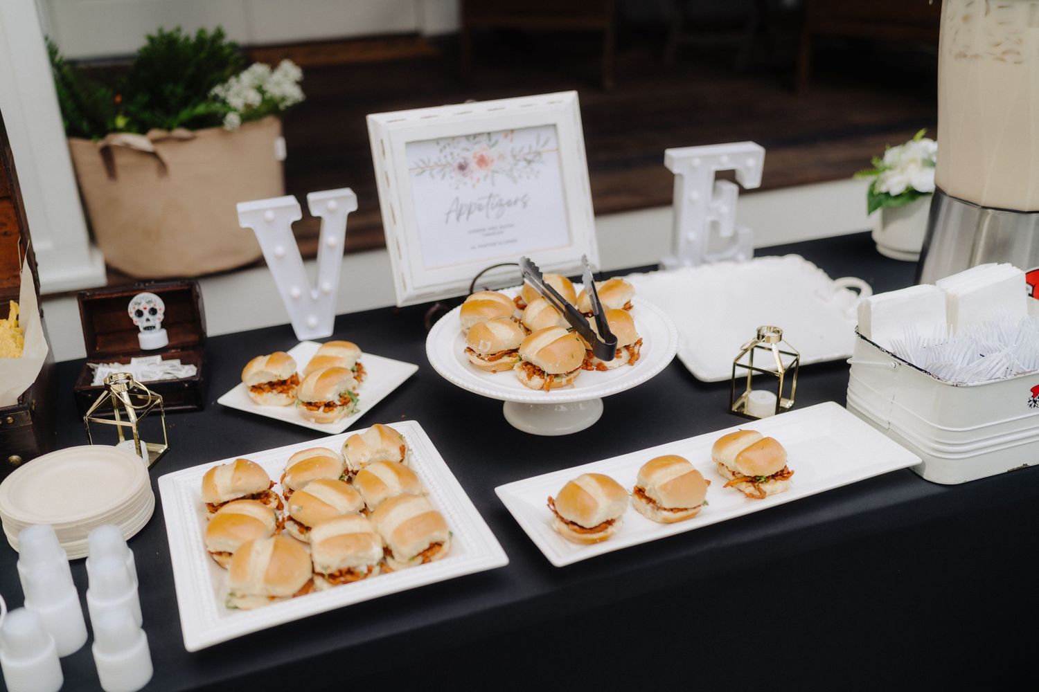 Wedding dessert table with white plates of cookies and treats arranged on a black tablecloth.