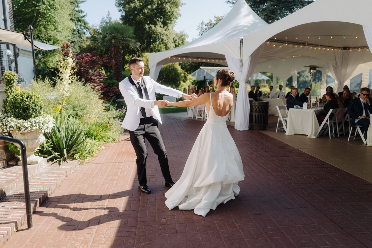 Outdoor wedding ceremony under white tents on a brick pathway surrounded by greenery.