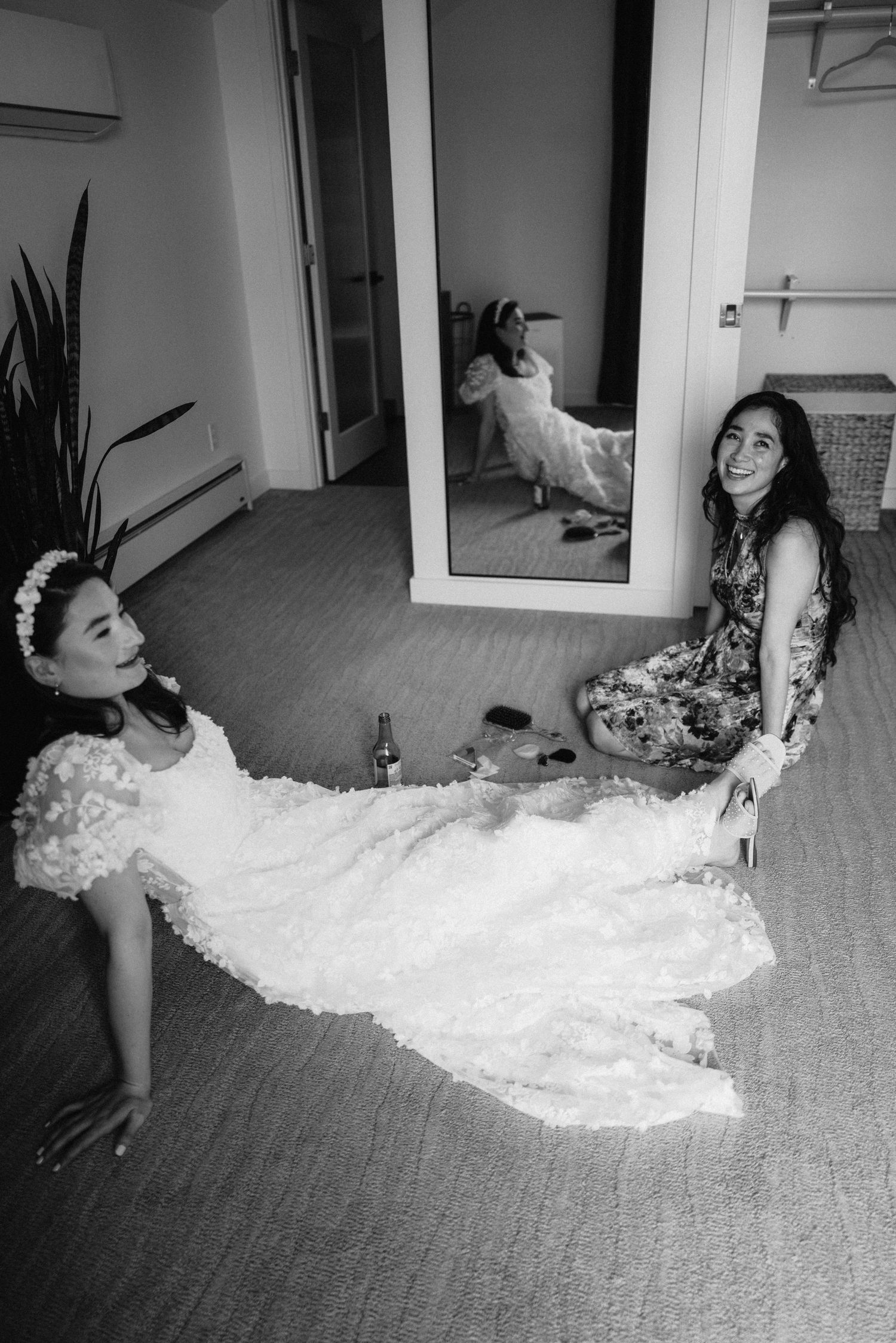 A flowing white wedding dress spreads elegantly across a carpeted floor in an indoor photoshoot.