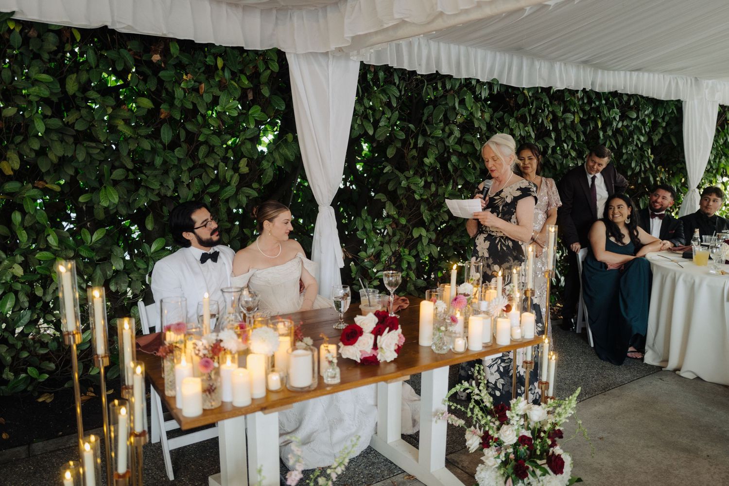 Elegant wedding reception decor with white draping and glowing candles on rustic tables.