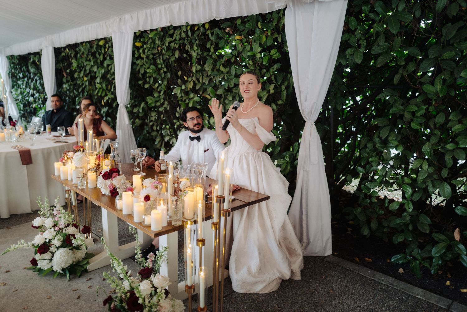 Intimate wedding reception space with white tent draping and natural green wall backdrop.