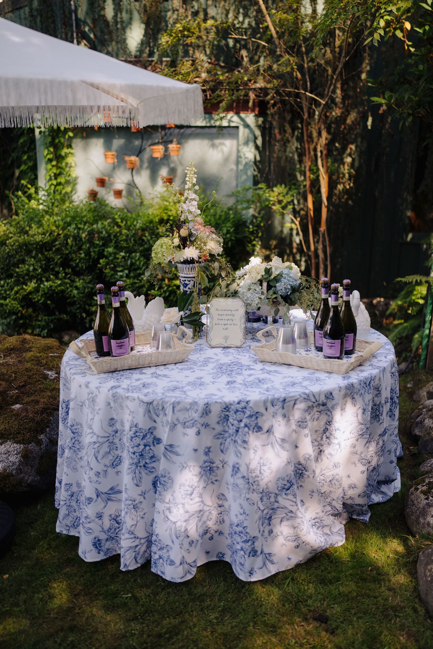 Elegant wedding reception tables decorated with blue and white toile tablecloths in an outdoor garden setting.