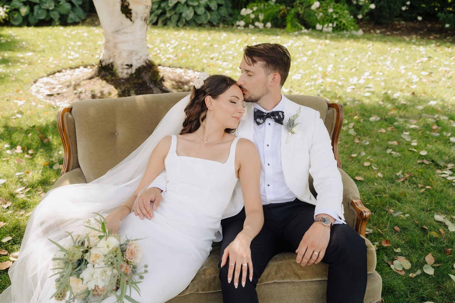 A couple relaxes on a white blanket in a lush garden setting during their wedding photoshoot.