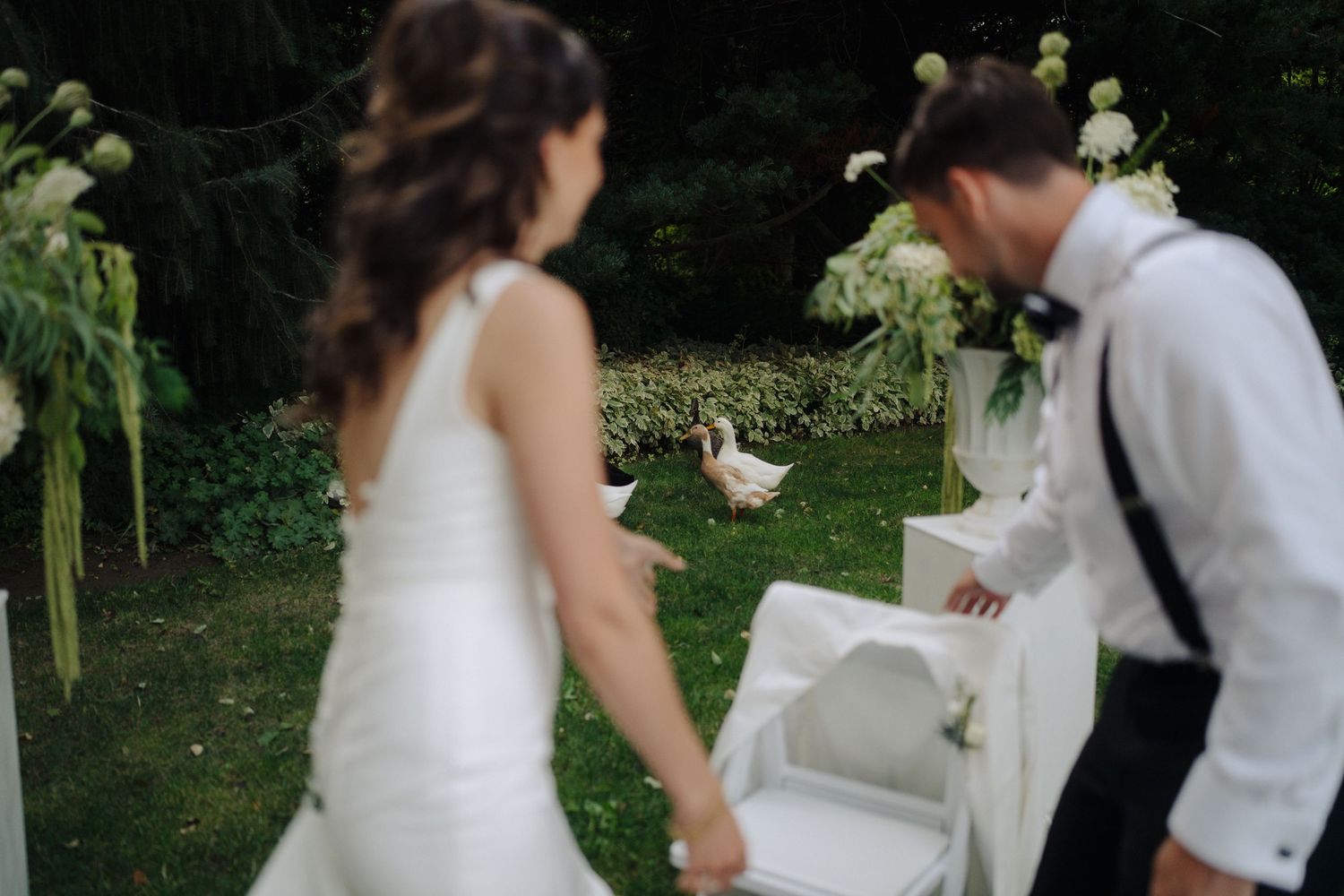 Couple celebrating at outdoor wedding reception with decorative white birdcage in garden setting.
