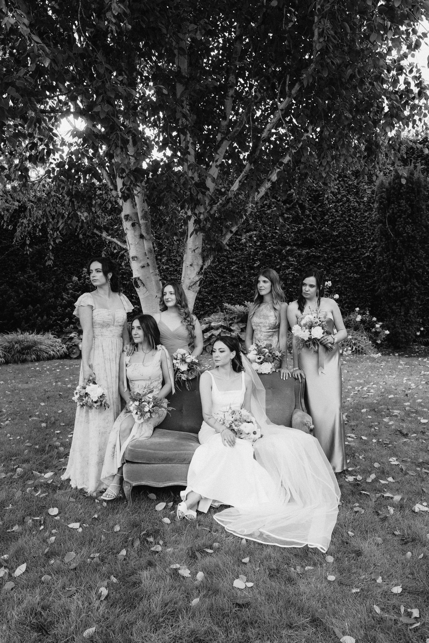 Wedding party relaxes on garden benches during outdoor photo session.