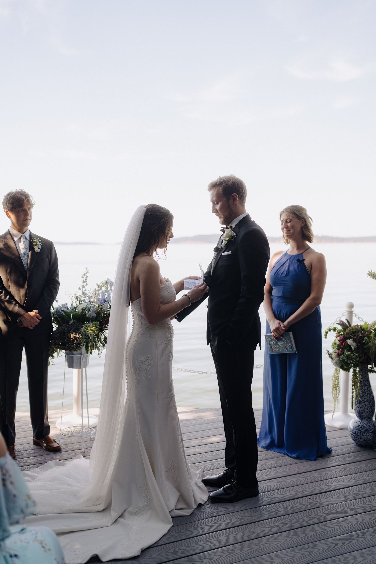 Intimate waterfront wedding ceremony taking place on a wooden deck overlooking the ocean.