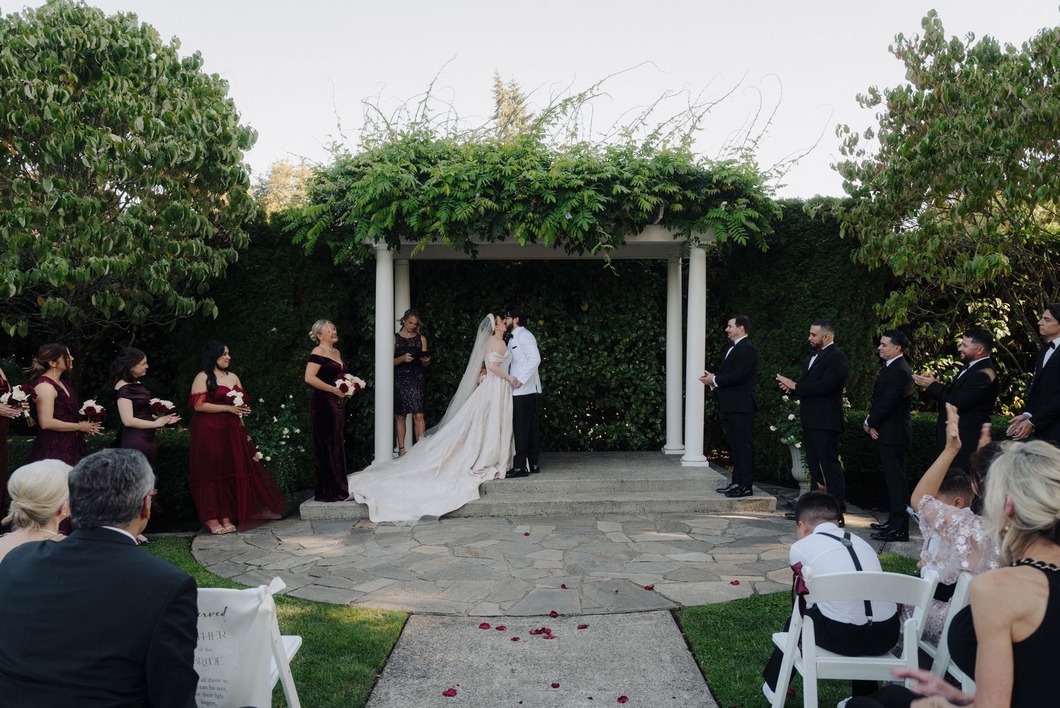 Wedding ceremony taking place in an elegant outdoor garden setting with white chairs and floral arrangements.