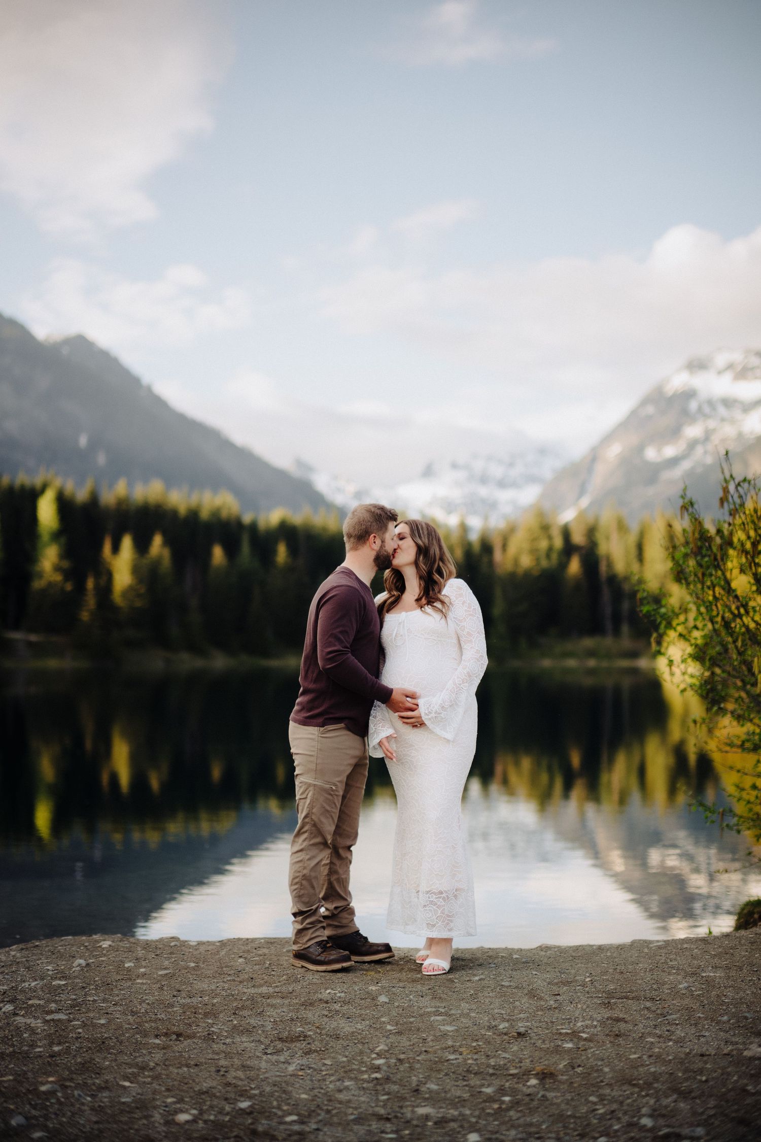 Romantic lakeside engagement photos with mountain and forest backdrop.