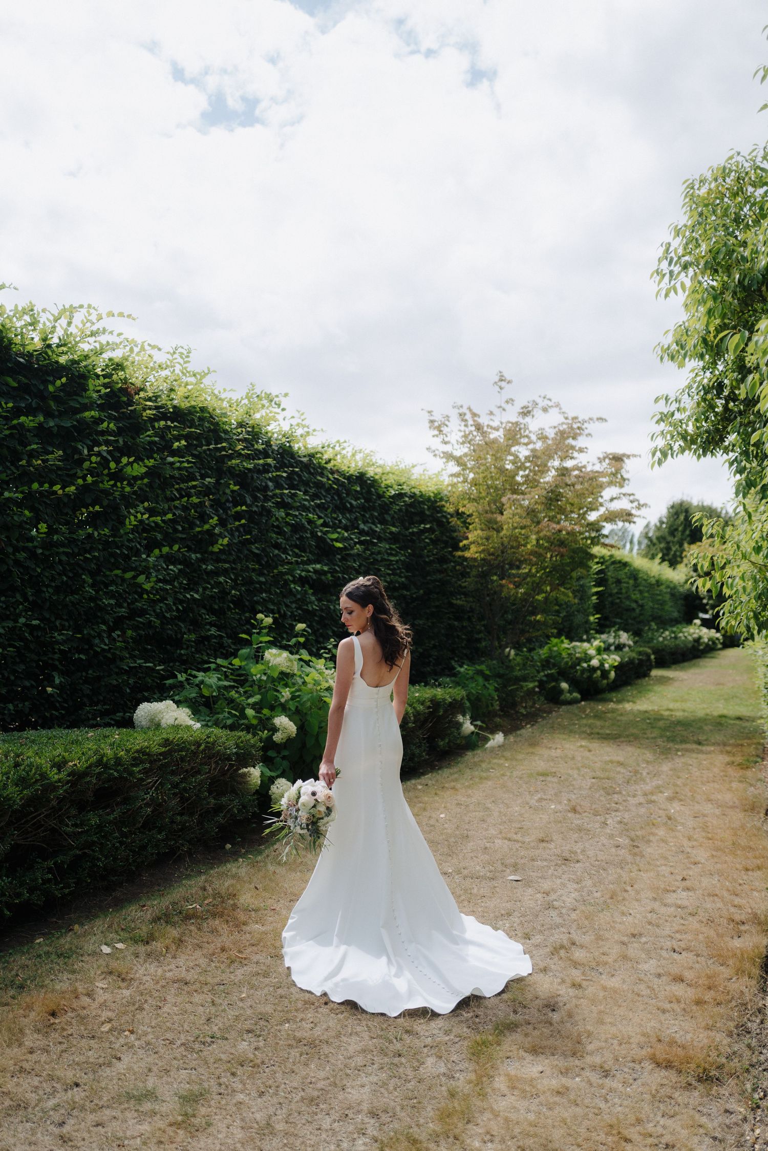 A white wedding dress twirls gracefully in an outdoor garden setting with green hedges in the background.