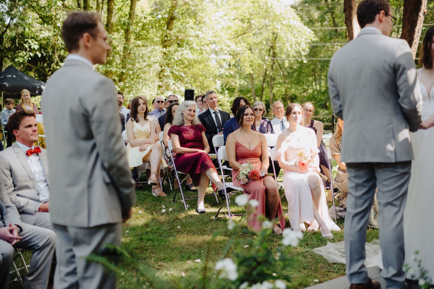 Wedding guests seated in white chairs watch the outdoor ceremony proceedings.