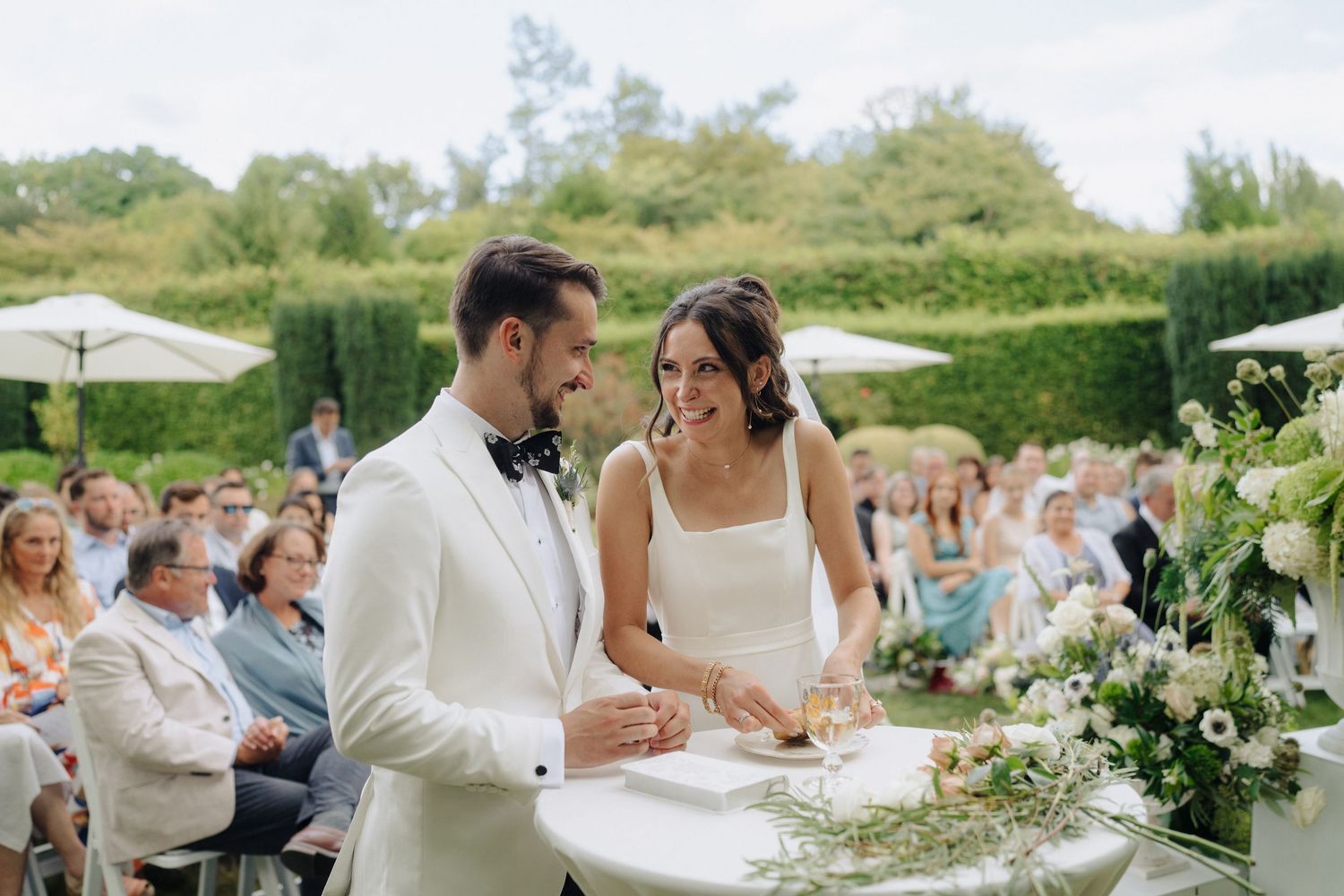 An elegant outdoor wedding reception with white floral arrangements and table settings.