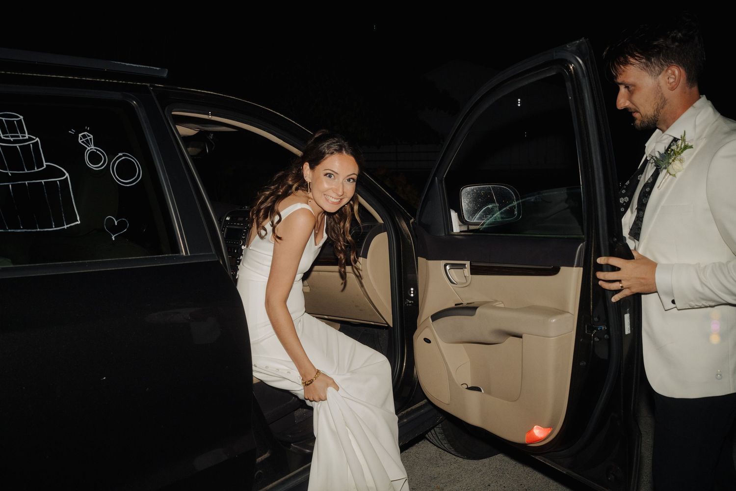 Wedding party members enter a vehicle during evening departure from celebration.