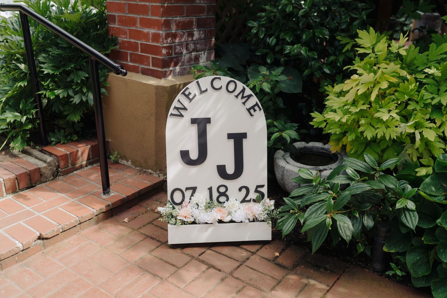 Decorative brick walkway with welcome signs and greenery at an outdoor wedding venue.