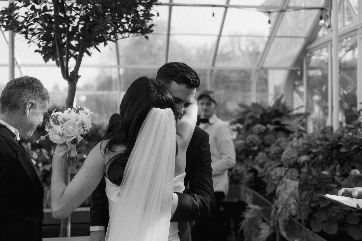 A black and white capture of an intimate wedding ceremony moment in a greenhouse setting.