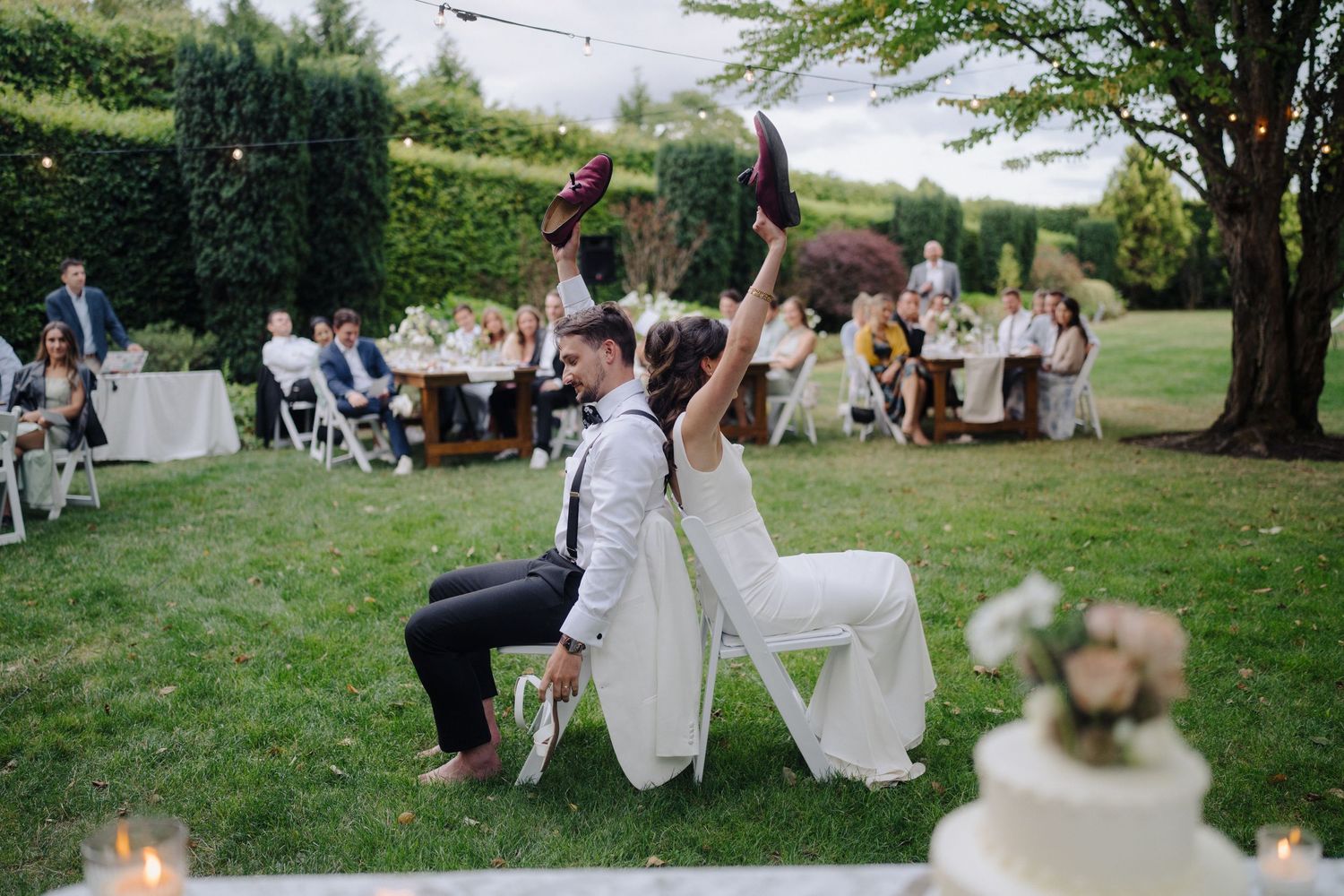 Outdoor wedding reception setup with white tables and chairs scattered across a sunny garden lawn.