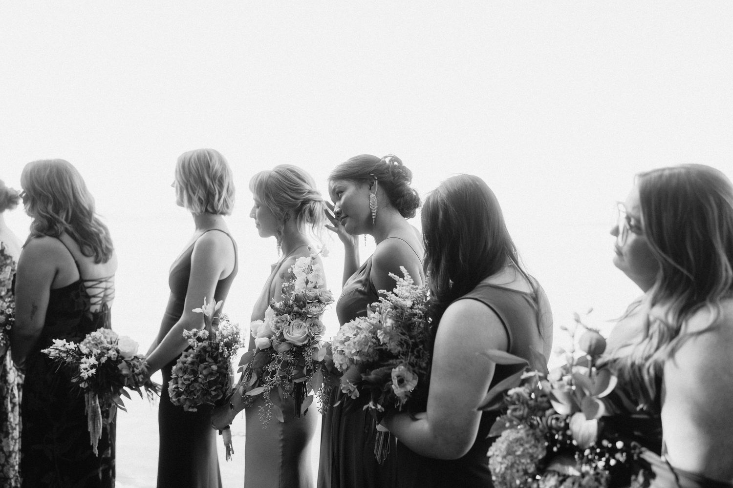 Black and white silhouettes of wedding guests standing in a row during an outdoor ceremony.