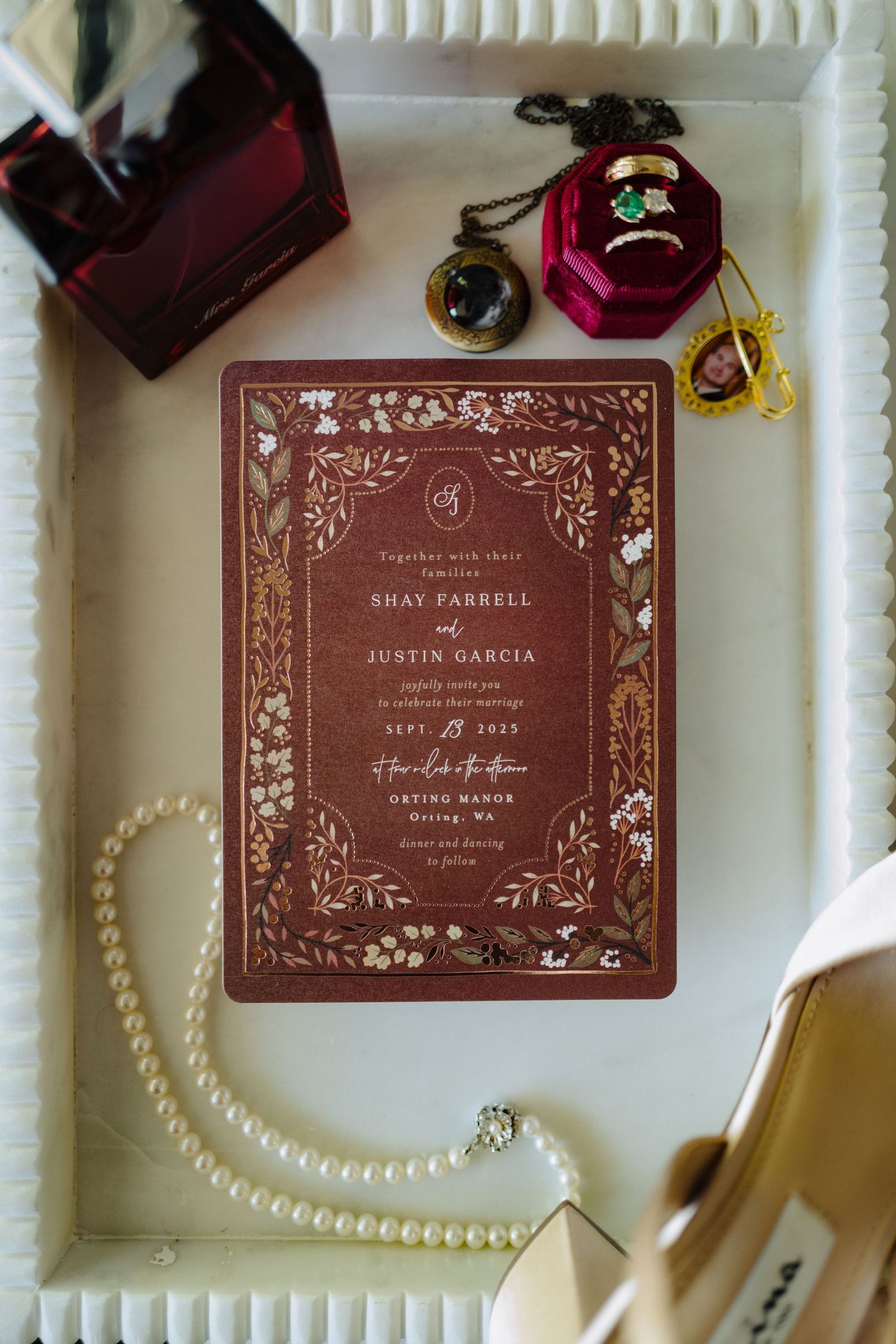 Elegant burgundy wedding invitations with floral designs displayed alongside pearl necklaces and decor details.