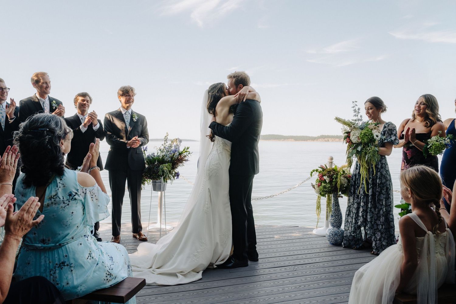 Wedding ceremony on a waterfront deck with guests seated in formal attire.