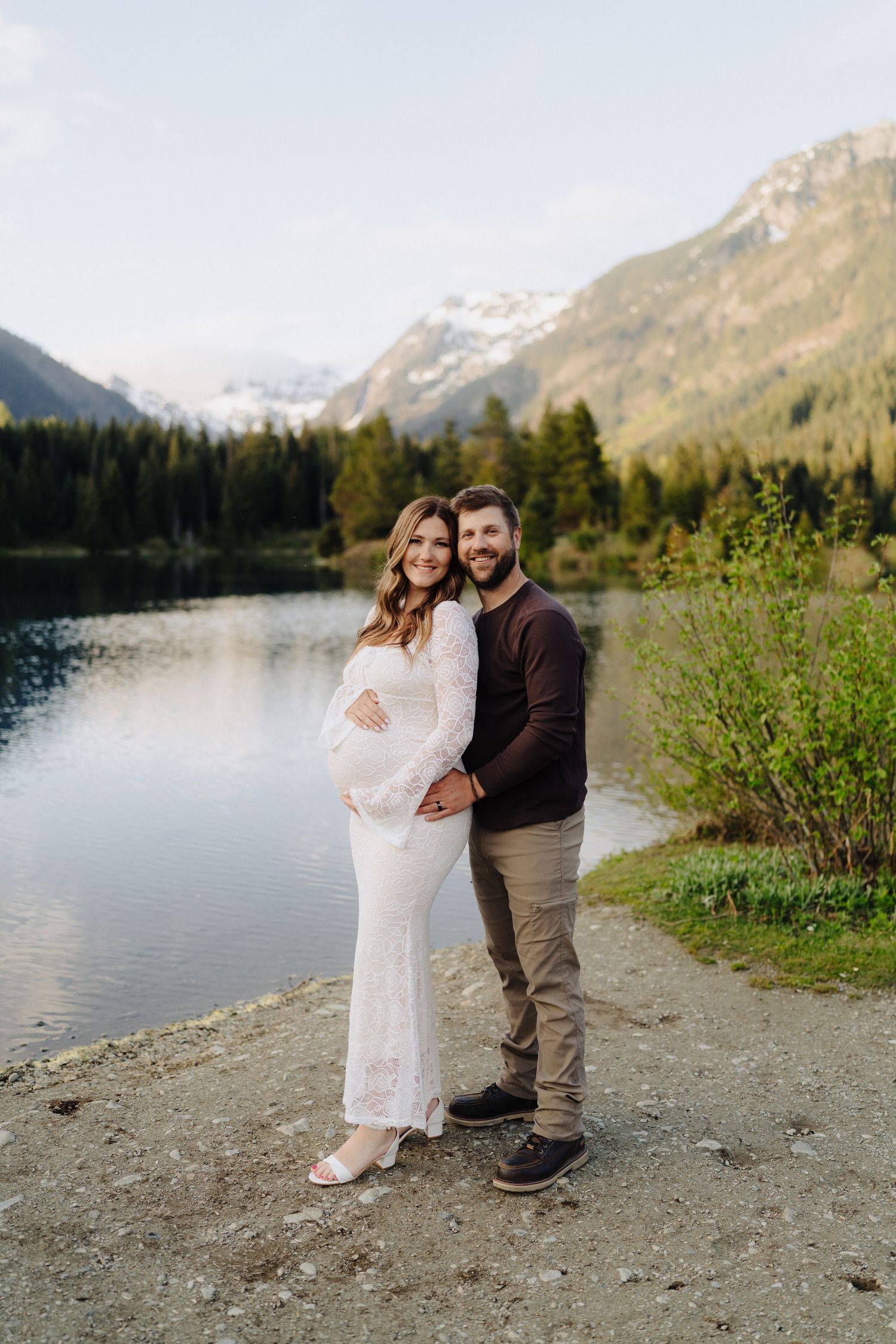 A maternity photoshoot against a backdrop of snow-capped mountains and a pristine lake.