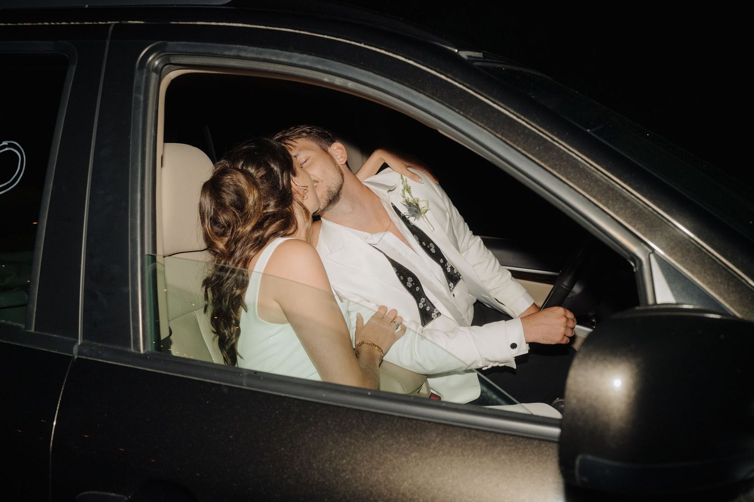 Wedding couple shares intimate moment in car at end of celebration.
