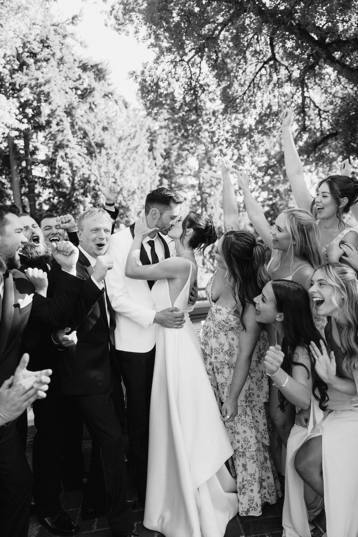 A joyful black and white photo of wedding guests celebrating and dancing together outdoors.