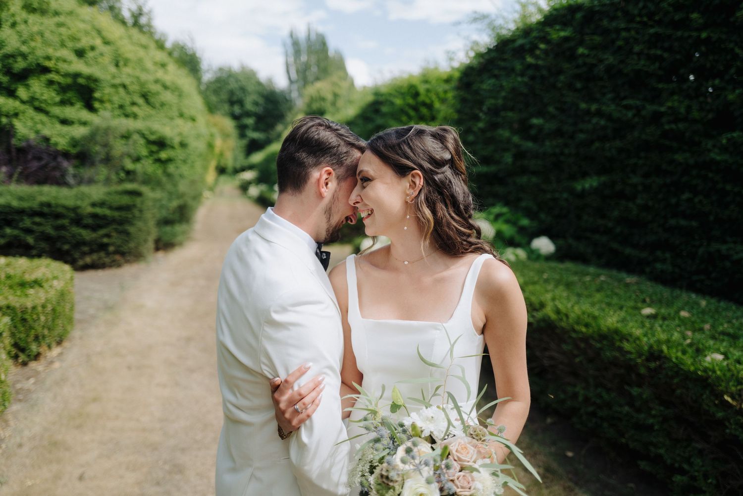 Couple strolling along a scenic garden path lined with tall hedges.