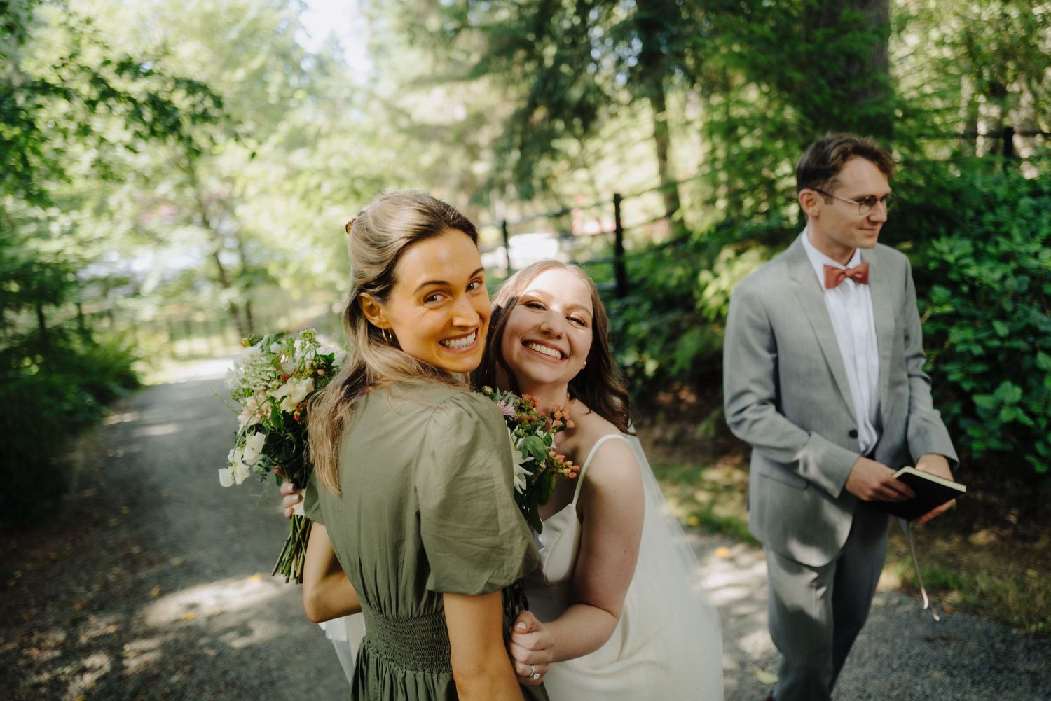 Wedding party poses together in a lush green forest setting wearing coordinated gray and burgundy attire.