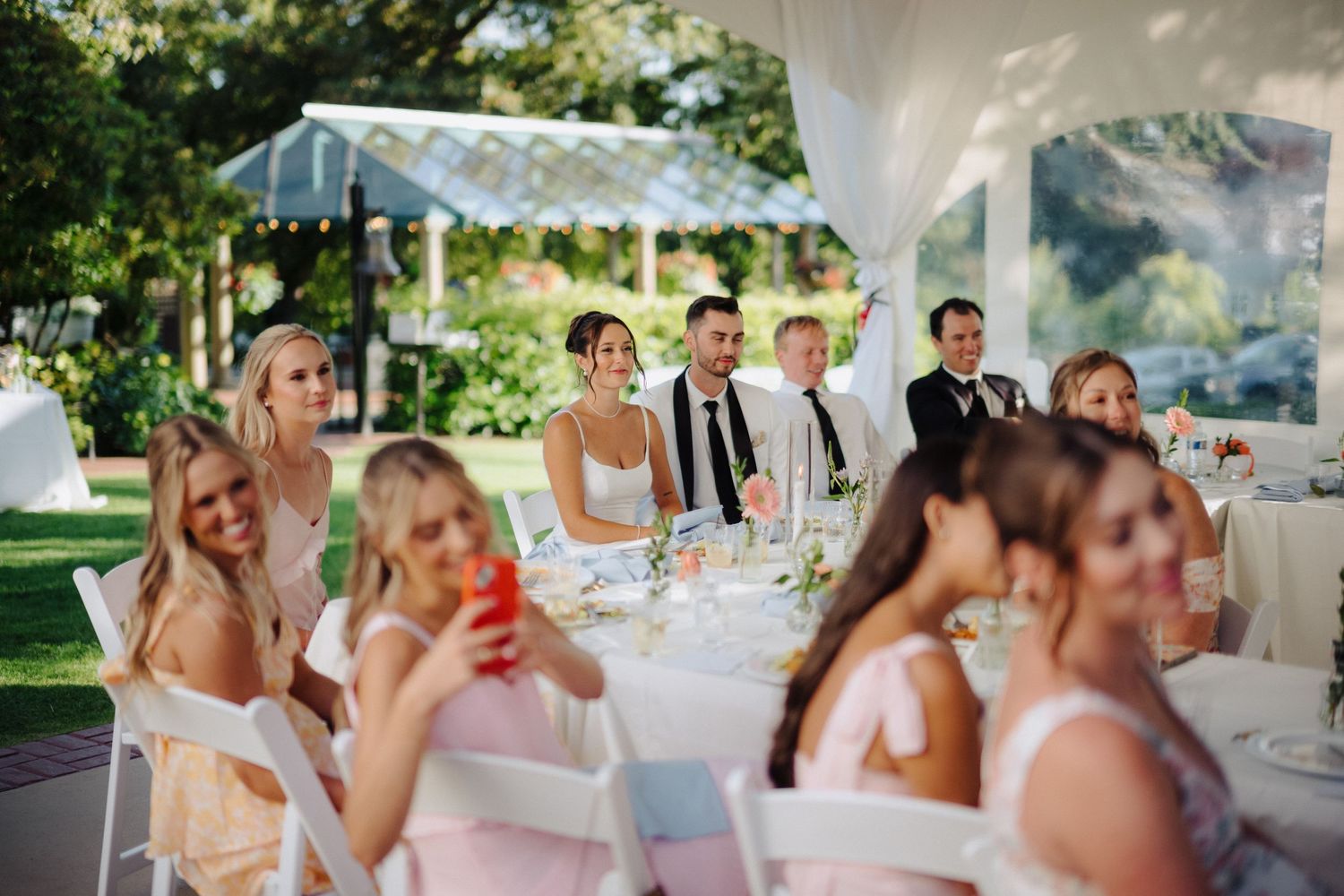 Wedding reception guests celebrating under white tent with outdoor garden views.