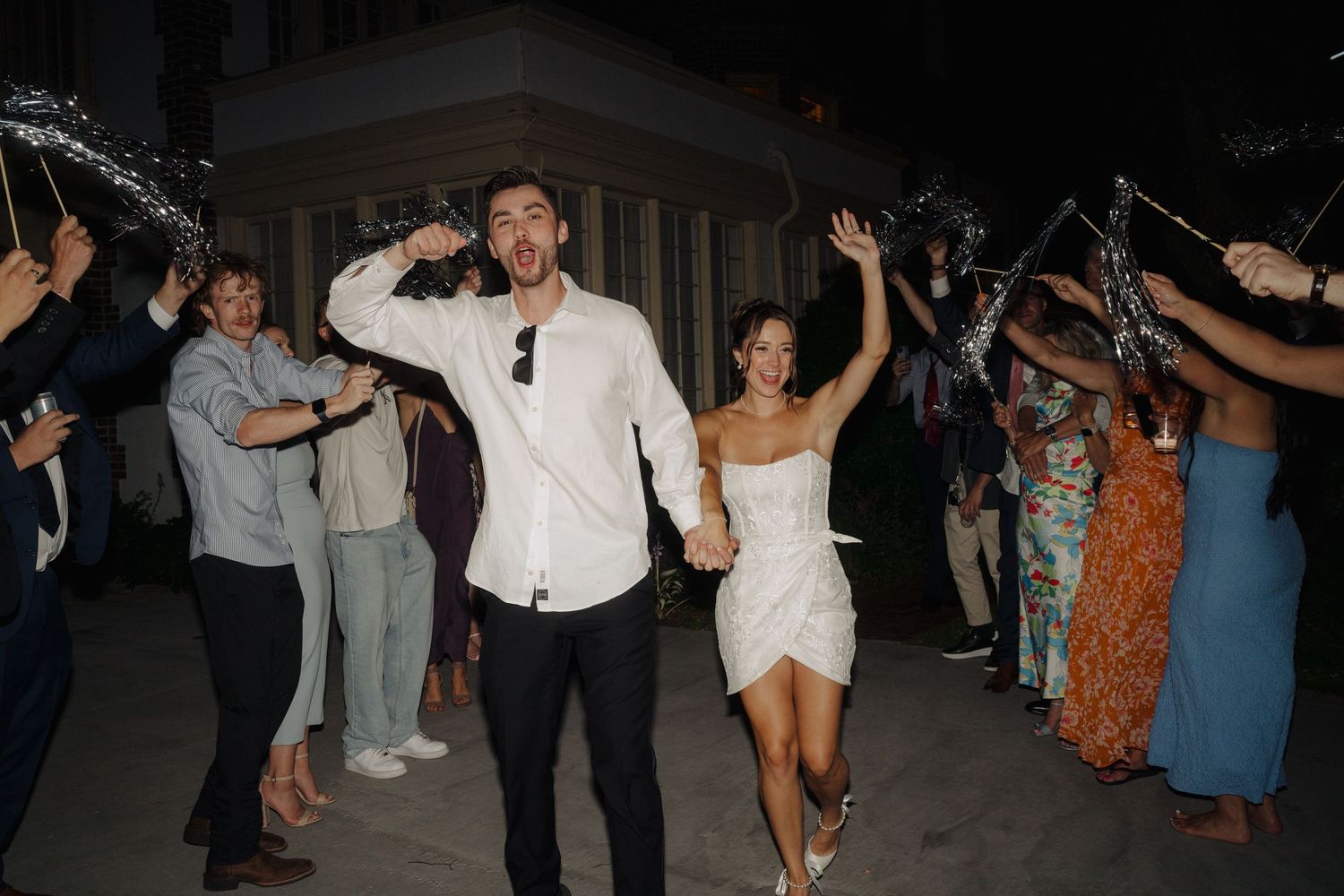Wedding guests forming a dance line during an outdoor evening reception.