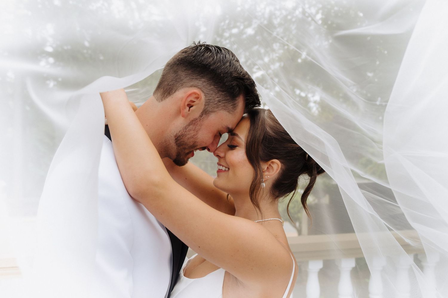 Romantic wedding couple embracing under a flowing white veil during their special day.