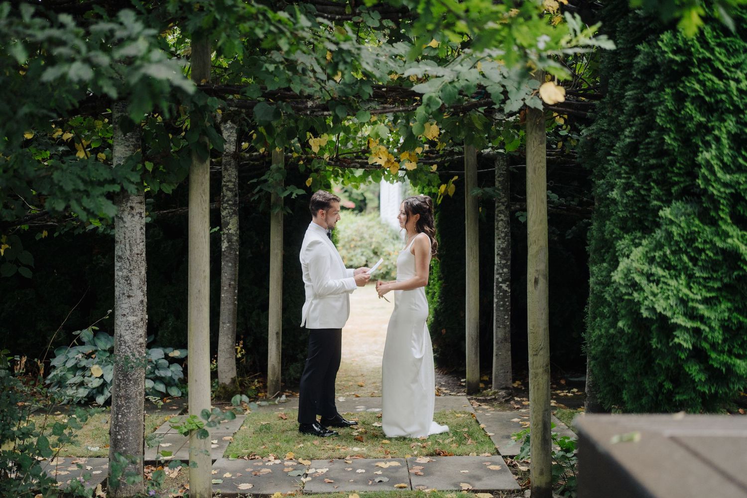Garden wedding ceremony setup with white chairs and floral arrangements along a tree-lined path.