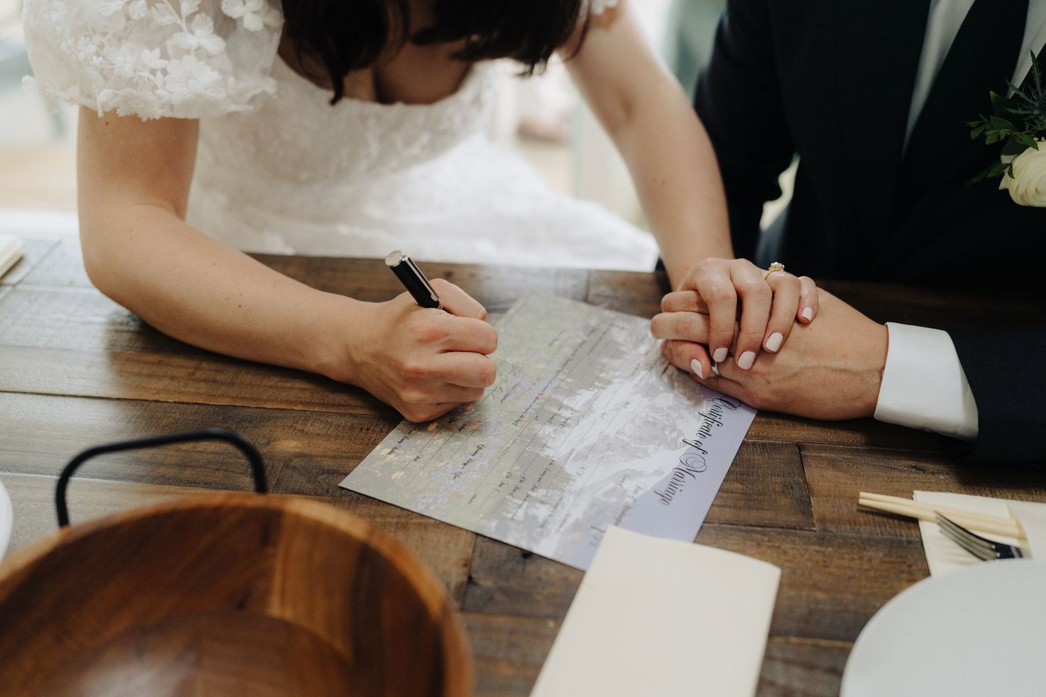 Wedding guests signing documents at a wooden table during a ceremony.