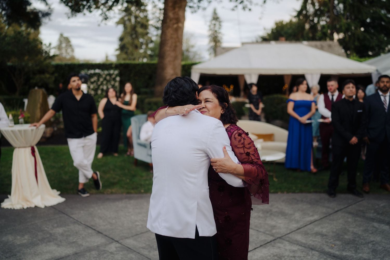 Guests watch as couples share dances at an outdoor wedding reception with string lights overhead.