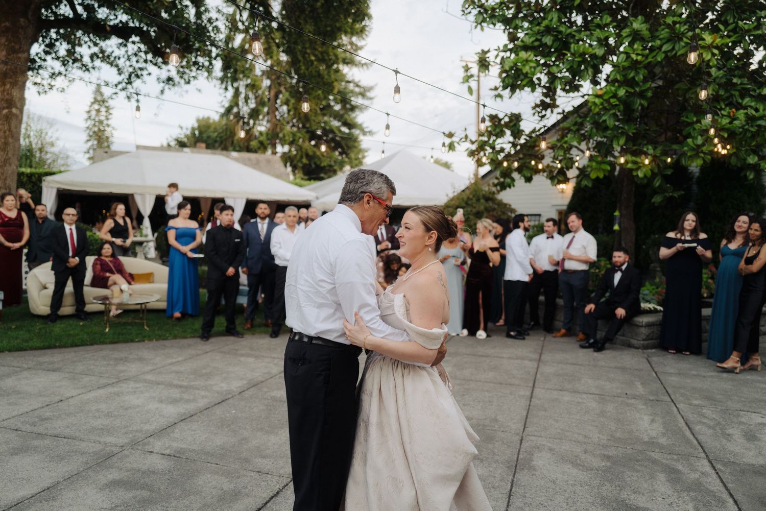 Garden wedding reception space decorated with overhead string lights and white tent canopies.