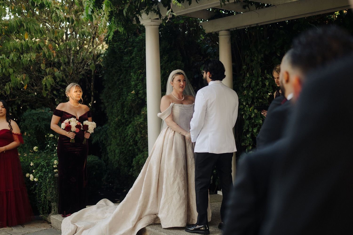 Wedding guests gather outdoors for a celebration beneath green foliage and string lights.