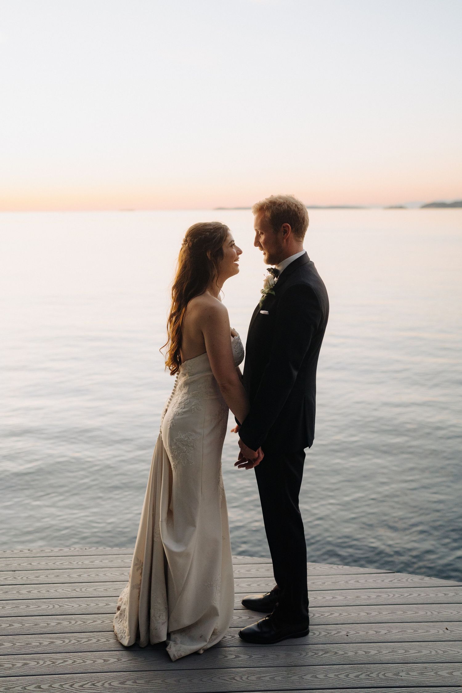 Couple shares intimate moment on wooden deck overlooking calm waters at sunset.