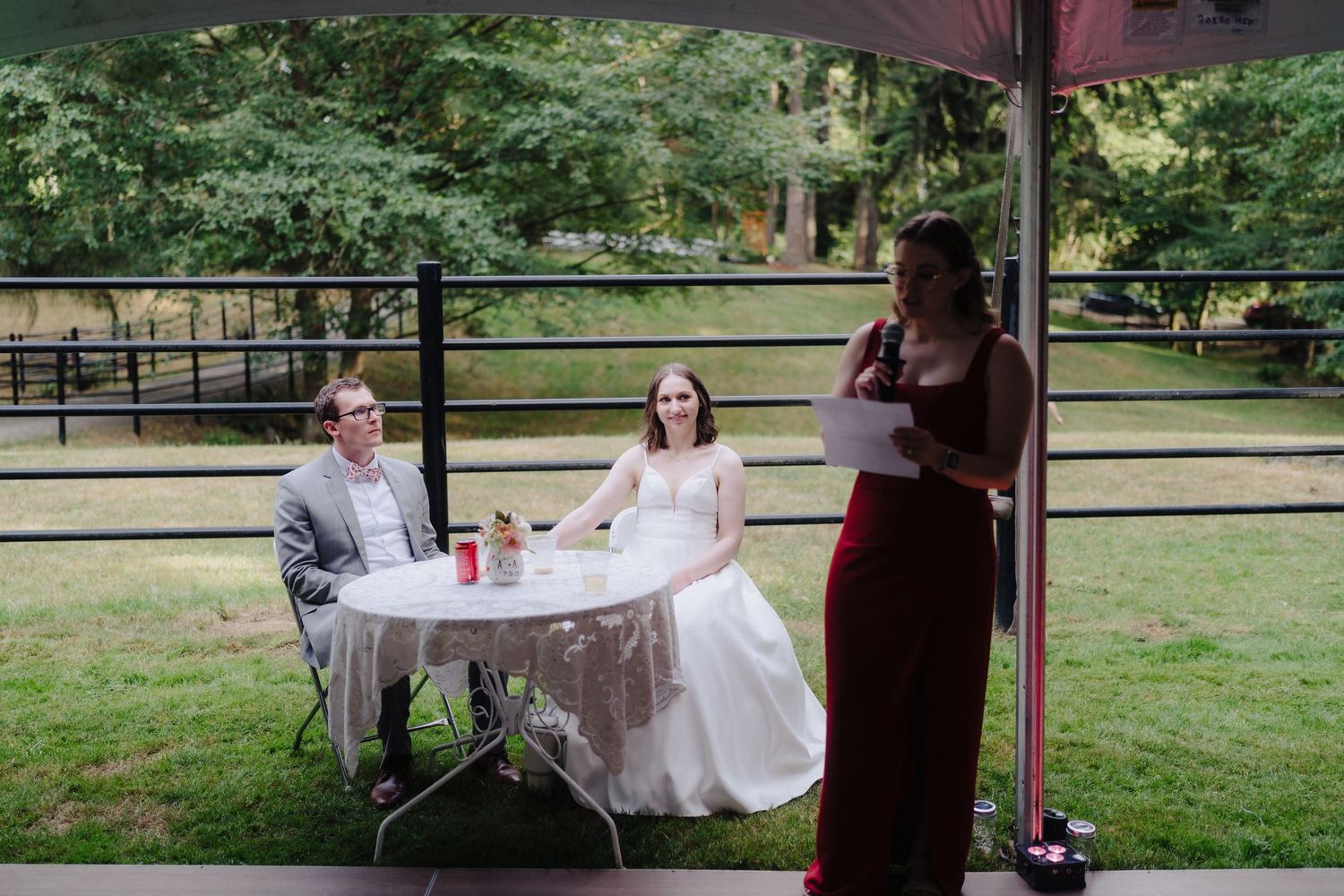 Outdoor wedding reception under tent with guests seated at tables near pastoral fence line.